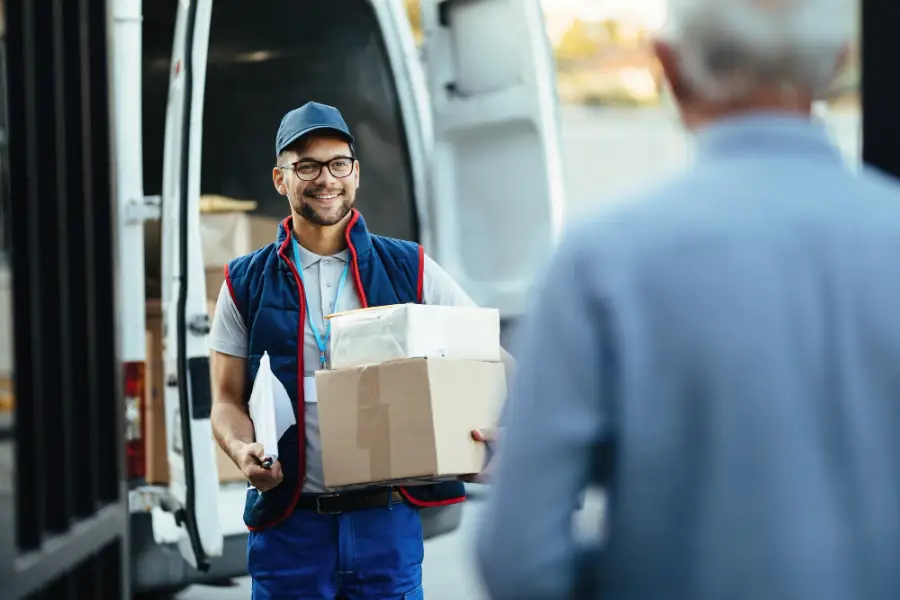 Happy deliverer carrying packages while making home delivery to his customer